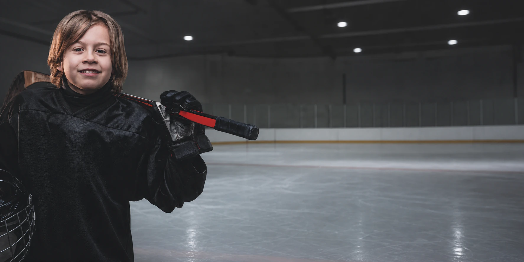 Kind in Hockeyausrüstung am Rand eines Eisfelds